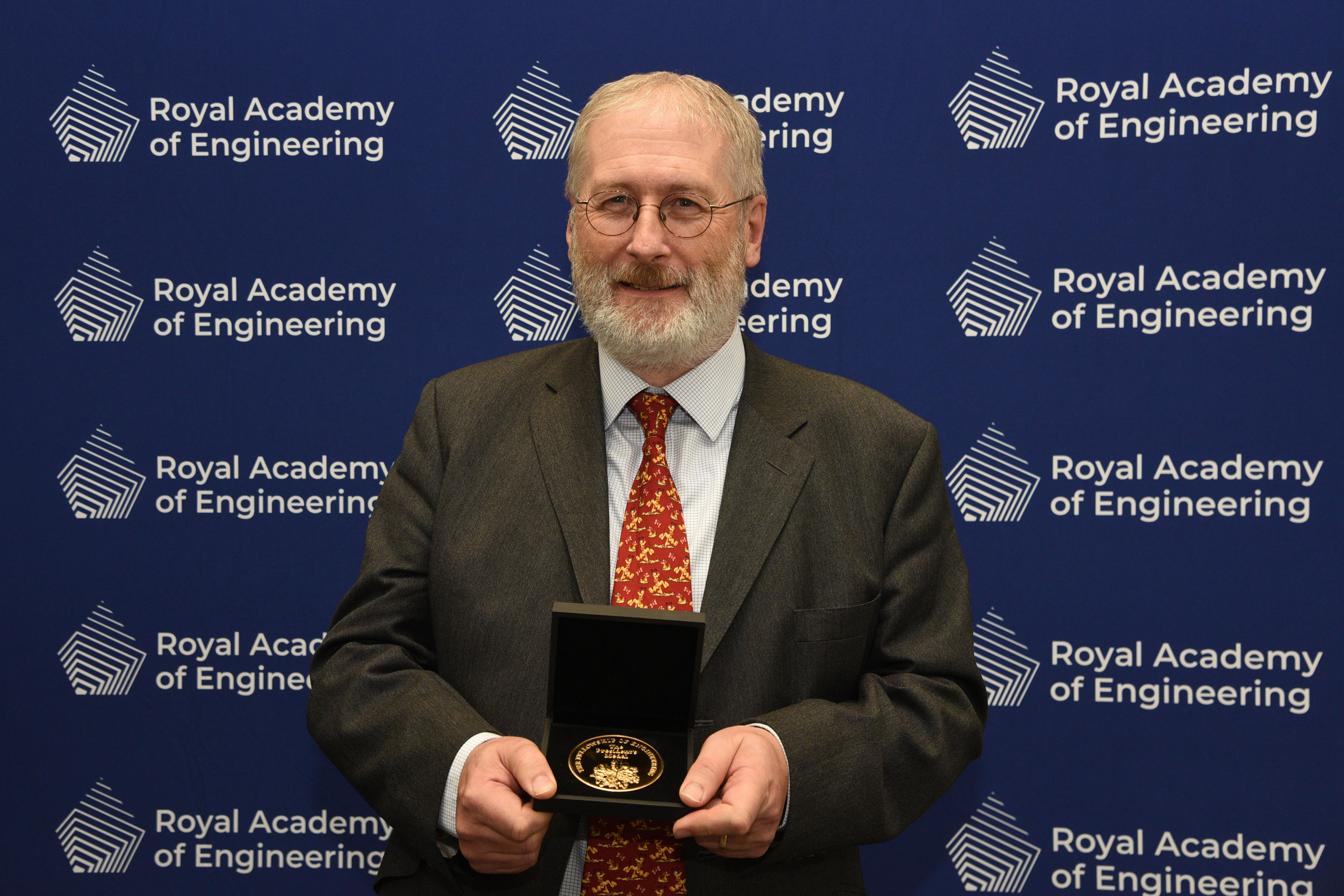 Professor John Clarkson FREng holding his President's Medal in front of a blue screen with the Royal Academy of Engineering logo