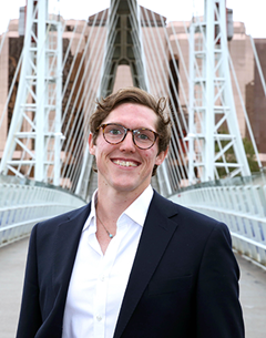 A man smiles at camera with a bridge in the background