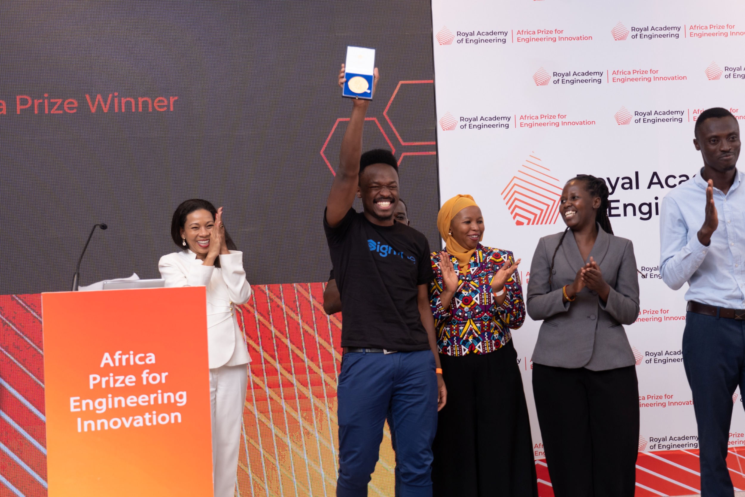 Africa Prize winner holding up an award on stage as colleagues applaud.