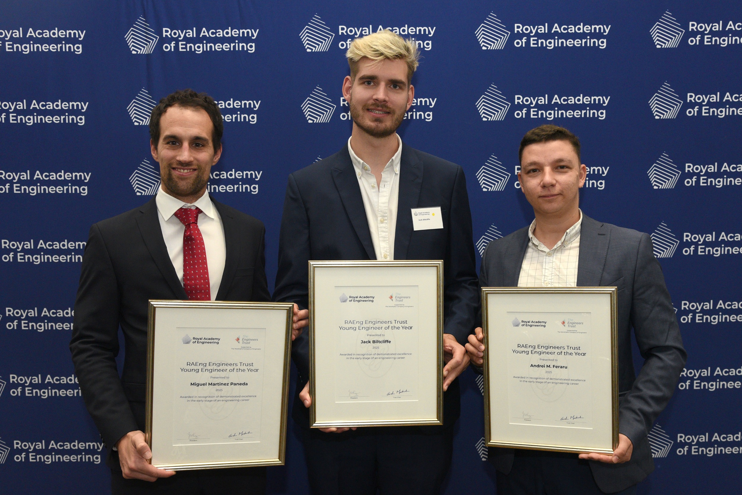 Three engineers in business attire hold certificates in front of a blue backdrop.