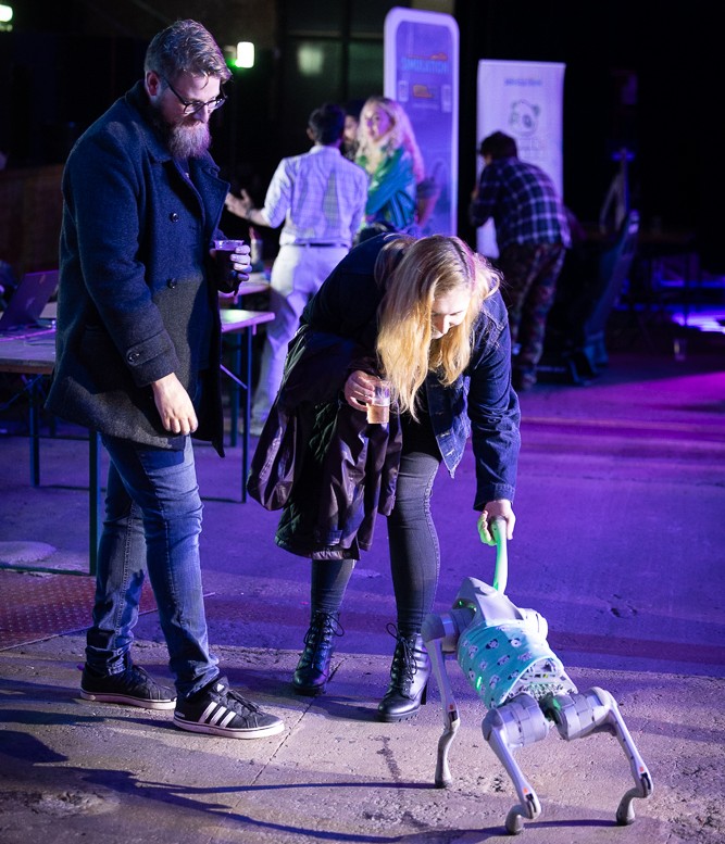 Two people leaning down to interact with a robotic dog.