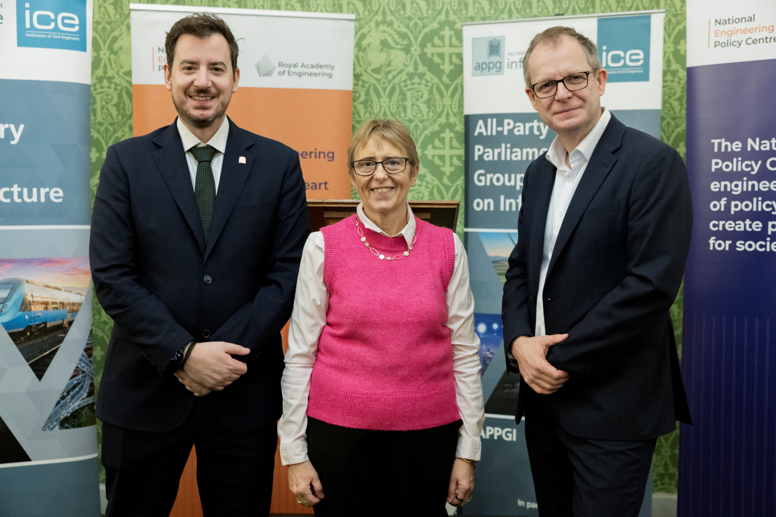 Three people posing for a photo in front of engineering and public policy event banners.