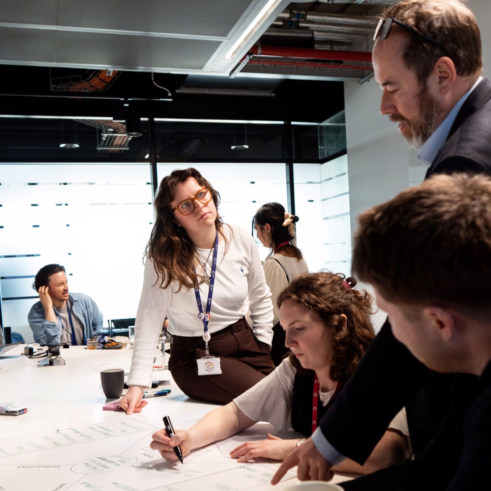 People collaborating around a table during a workshop, reviewing and writing on a large planning sheet in a meeting room.