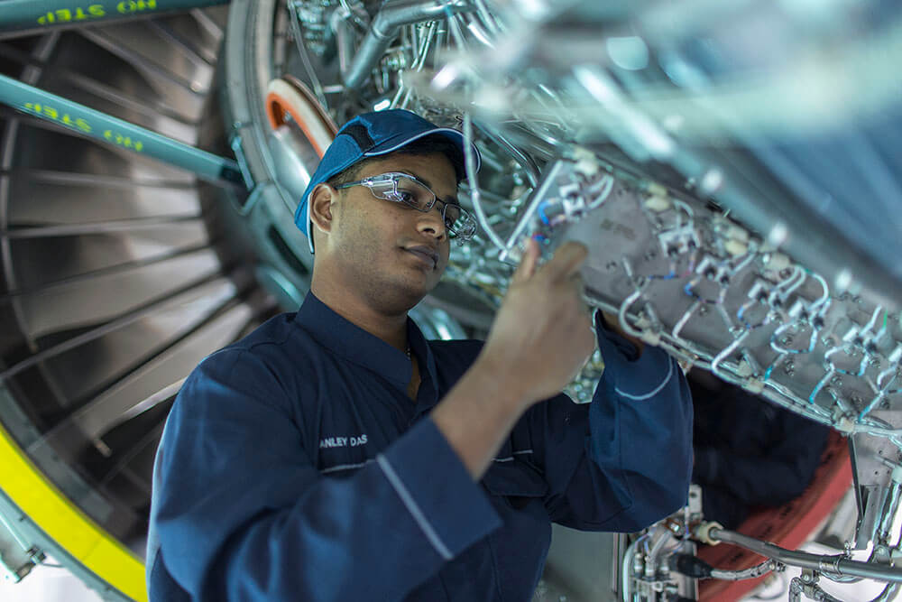 A man wearing a blue shirt inspects a component of a complex engineering system.