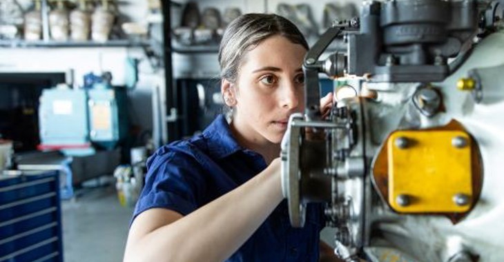 A Woman Works On A Machine Part In A Workshop
