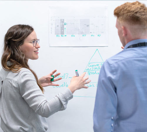 Couple of engineers discussing a project in front of a whiteboard.