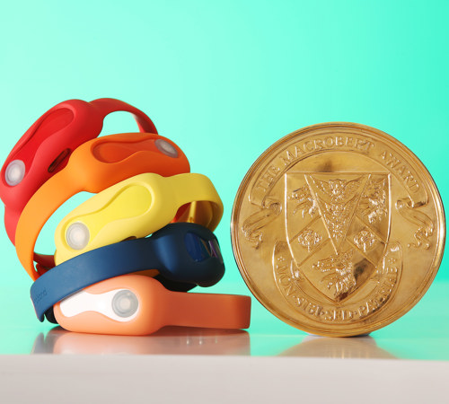 A stack of coloured DnaNudge wristbands next to a MacRobert Award medal
