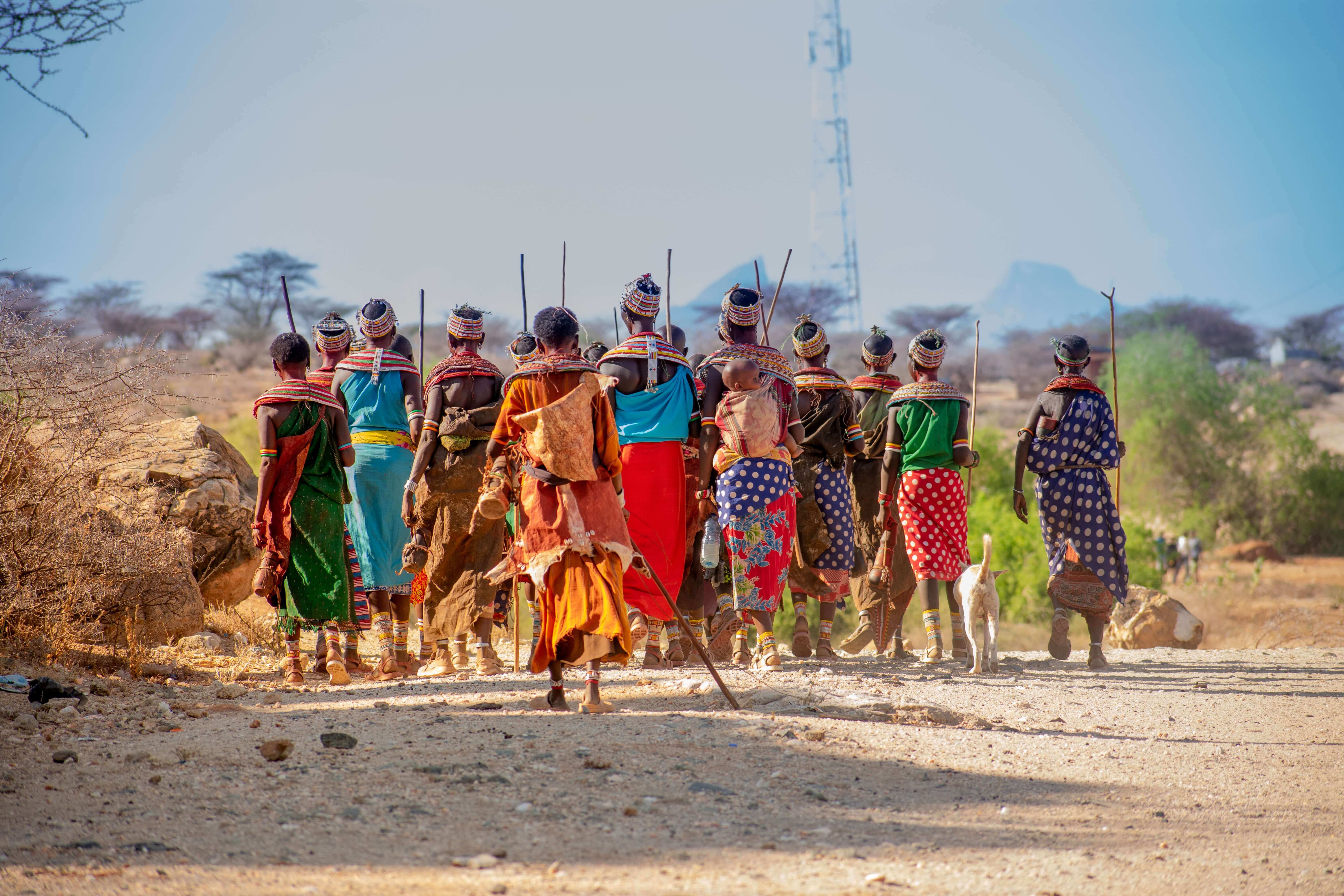 Group of tribespeople walking away in sunshine and over sandy landscape