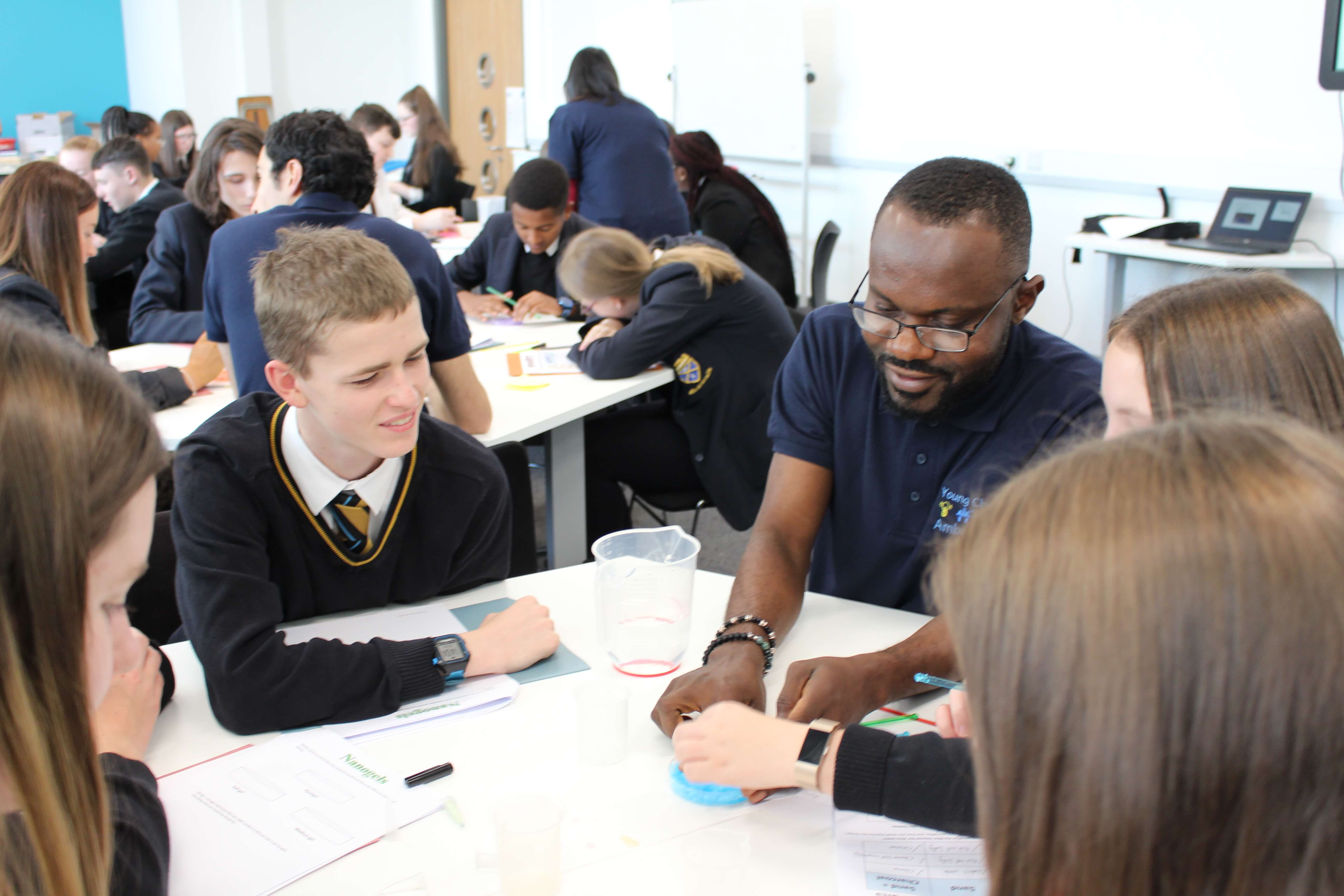A picture showing school students round tables being led through an activity