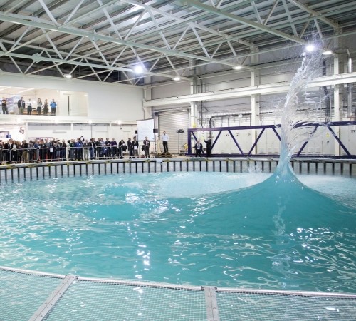 A group of people standing and watching a big wave in a pool