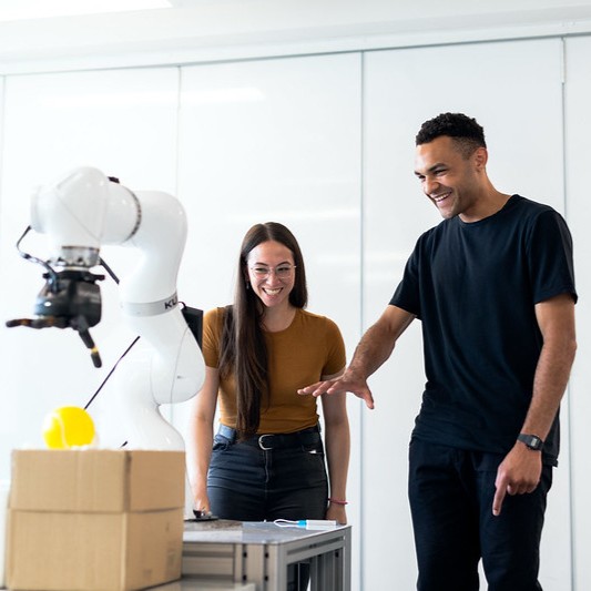 A man and a woman smiling as they look at engineering equipment.