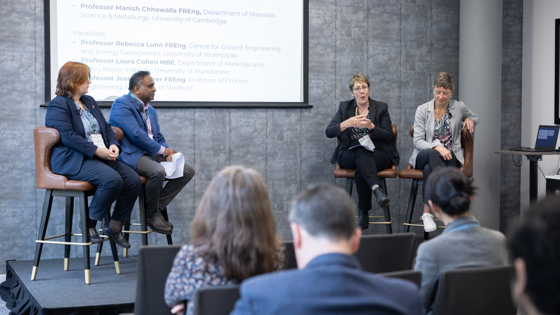Four panellists sit on a stage with a screen behind them which says 'Panel discussion: Critical materials'