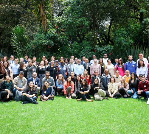 Large group photo of international participants standing and sitting in a garden.